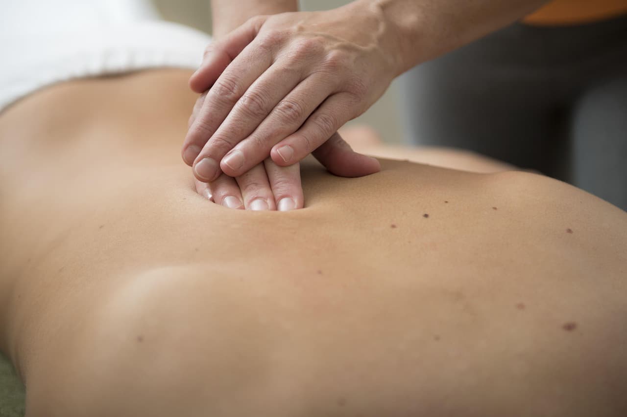 Physiotherapist pressing into the muscles of a patient's upper back